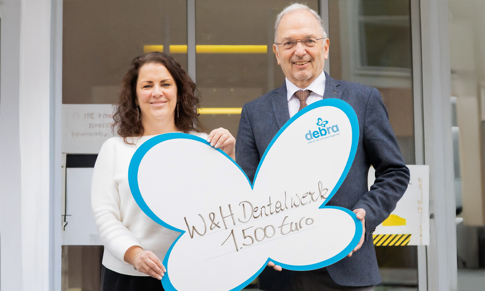 Elisabeth Rettenbacher (EB House Austria) and Peter Malata (W&H Dentalwerk Bürmoos GmbH) smiling at the camera, handing over the donation.