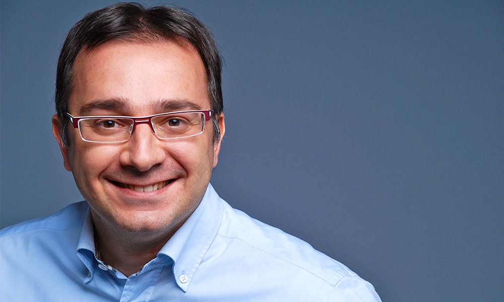 Dr Trasarti smiling in the camera in front of a blue backround.