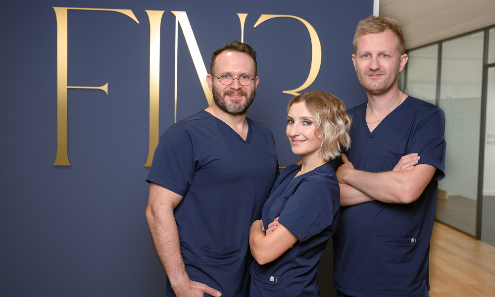 El Dr. Tudor Sandulescu, la Dra. Iryna Hermes y el Dr. Marc Hermes sonríen a la cámara delante de su nuevo logotipo.