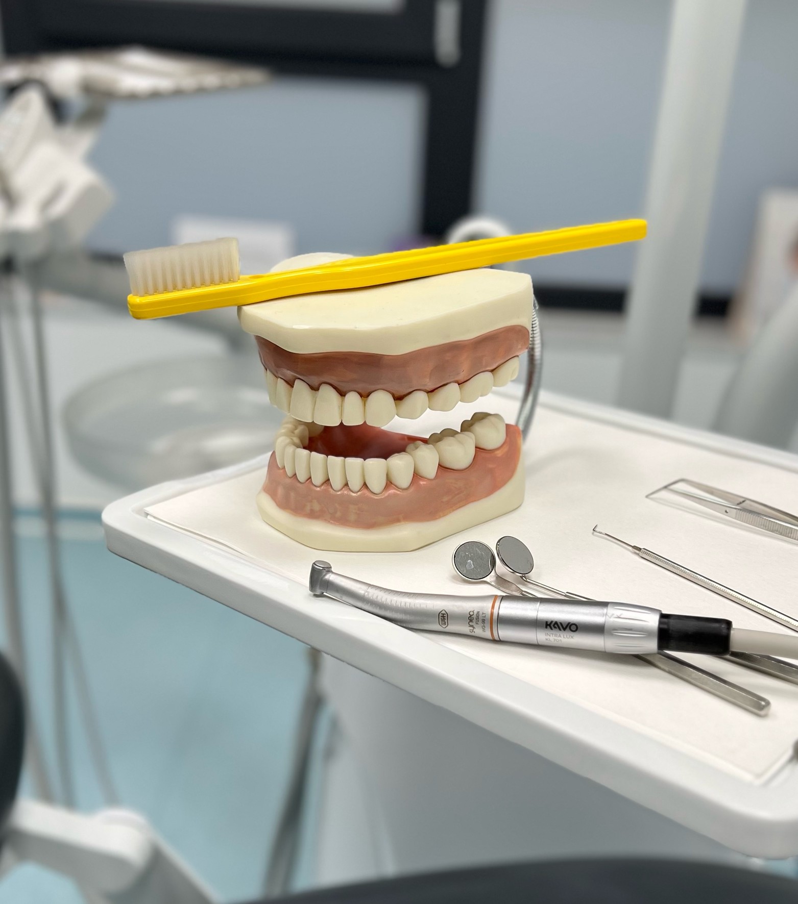 Conjunto de dientes artificiales con un cepillo de dientes amarillo y una pieza de mano Synea Fusion de W&H sobre una bandeja de tratamiento.