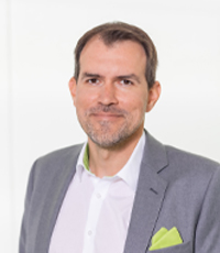 Thomas Lang smiling at the camera in front of a white background.