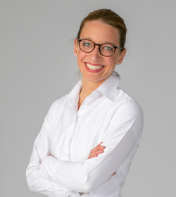Dr Romana Krapf MSC. smiling in the camera in front of a grey background.