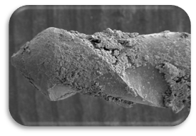 Une lime endodontique usagée non nettoyée, agrandie 100 fois, sur un fond gris foncé