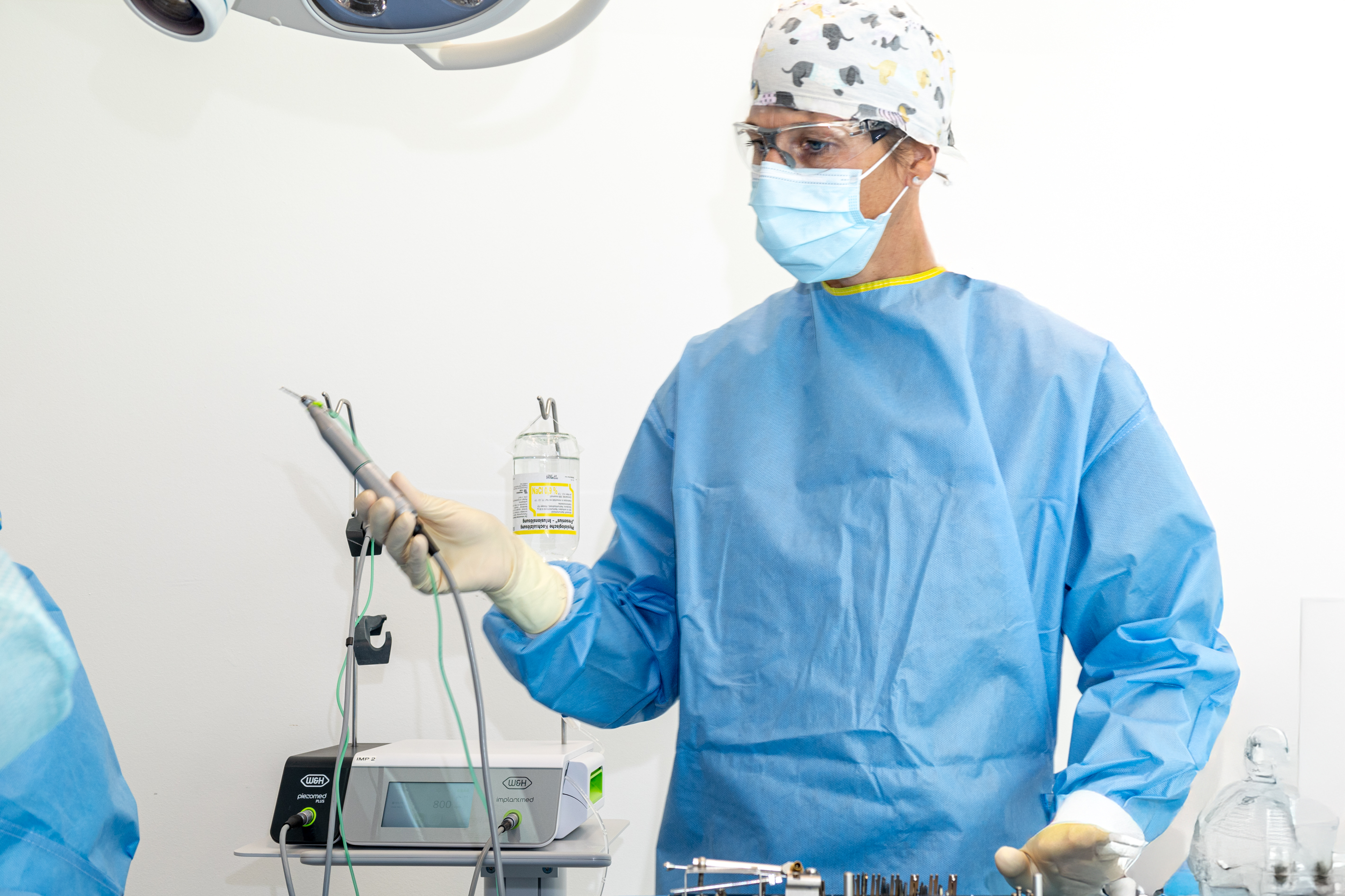 DDr. Manschiebel hält einen chirurgischen Motor vor einem Implantmed- und Piezomed-Modul.