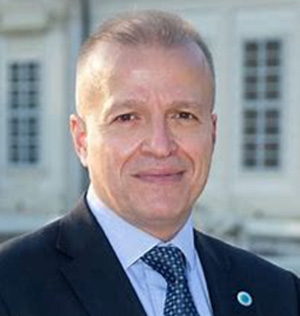 Prof. Dr. Andreas Stavropoulos lächelt in die Kamera, im Hintergrund ein Gebäude.