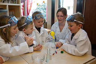 In einem Experiment spüren die Kinder des Kindergartens Schalchen (v.li.n.re.) Amelie Kogler, Dominik Junghuber, Alexander Moser und Paul Wallner gemeinsam mit Kindergartenpädagogin Maria Zauner den Eigenschaften des Germs nach. Vermischt mit Zucker, Mehl und warmem Wasser wird ein über eine Flasche gestülpter Ballon langsam aufgeblasen.