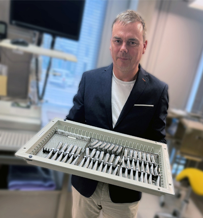 Dr. Frank Tolsdorf ține în mână o tavă plină cu piese de mână drepte și contraunghi din gama Synea Fusion, într-un cadru de laborator.