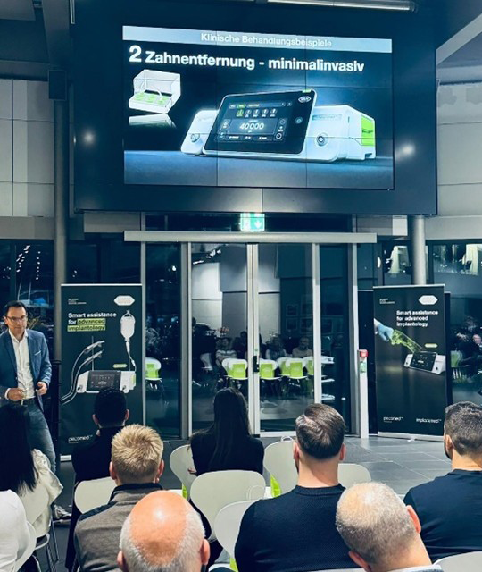 Audience attending a presentation by Dr med. dent. Frederic Hermann with a large screen showing the new Implantmed Plus II.