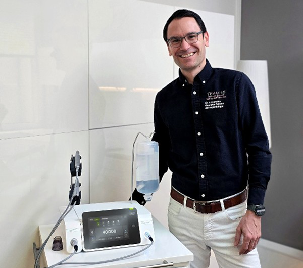 Dr. med. dent. Frederic Hermann mit dem Implantmed Plus II von W&H in seiner Praxis lächelt in die Kamera.