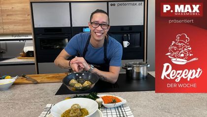 Ein lächelnder Peter Lehner bereitet in einer modernen Küche Semmelknödel in einer Pfanne zu. Im Vordergrund ist der fertig angerichtete cremige Linseneintopf mit Knödeln sowie Schalen mit roten Linsen und frischen Kräutern zu sehen.