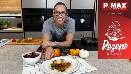 Kochprofi Peter Lehner präsentiert das fertig angerichtete Gericht: aufgeschnittene Hühnerroulade mit Kürbisgemüse auf einem weißen Teller. Auf der Arbeitsfläche der Küche liegen zudem frische Zutaten wie kleine Kürbisse und Radicchio sowie Kochutensilien bereit.