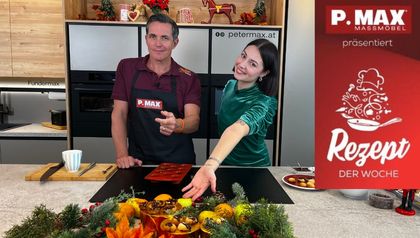 Philipp und Sarah stehen in einer Küche hinter einer Arbeitsfläche mit Backutensilien und präsentieren die fertig gebackenen veganen Florentiner und Kokos-Makronen, die festlich im Vordergrund angerichtet sind.