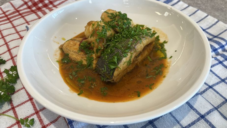 Original dalmatinische Fischsuppe in einer tiefen weißen Schüssel. Mehrere Fischstücke und einige helle, runde Klöße sind in einer orange-braunen Brühe angerichtet und großzügig mit frischer, gehackter Petersilie bestreut.