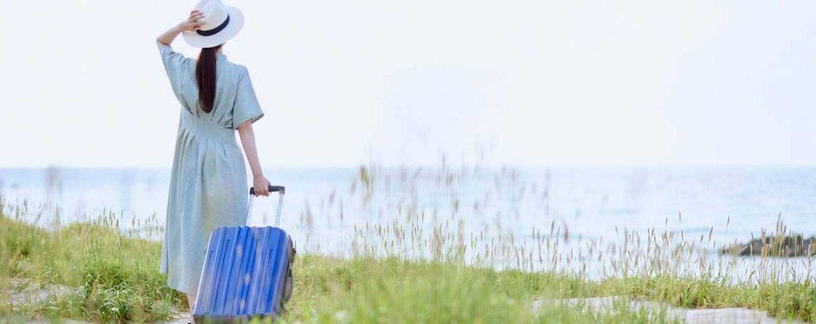 Femme de dos regarde la mer, une valise à la main
