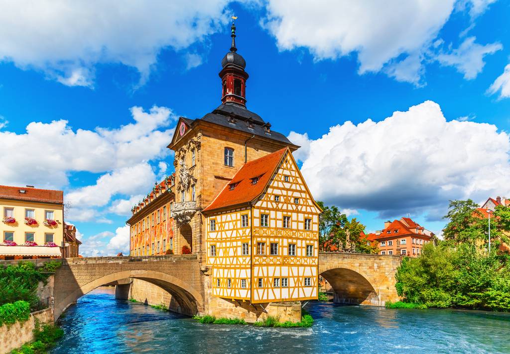Historisches Fachwerkgebäude auf einer Brücke über einem Fluss, unter einem teilweise bewölkten Himmel gelegen.
