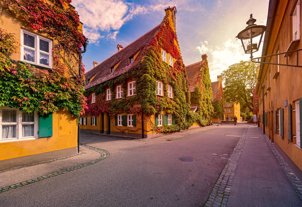 Ruhige europäische Straße bei Sonnenuntergang mit efeubewachsenen gelben Häusern, steilen Giebelhäusern, Kopfsteinpflaster-Bordstein und einer alten Straßenlaterne.