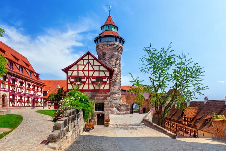 Blick auf die Nürnberger Burg mit Steinturm, Fachwerkhäusern und Kopfsteinpflasterweg unter blauem Himmel.