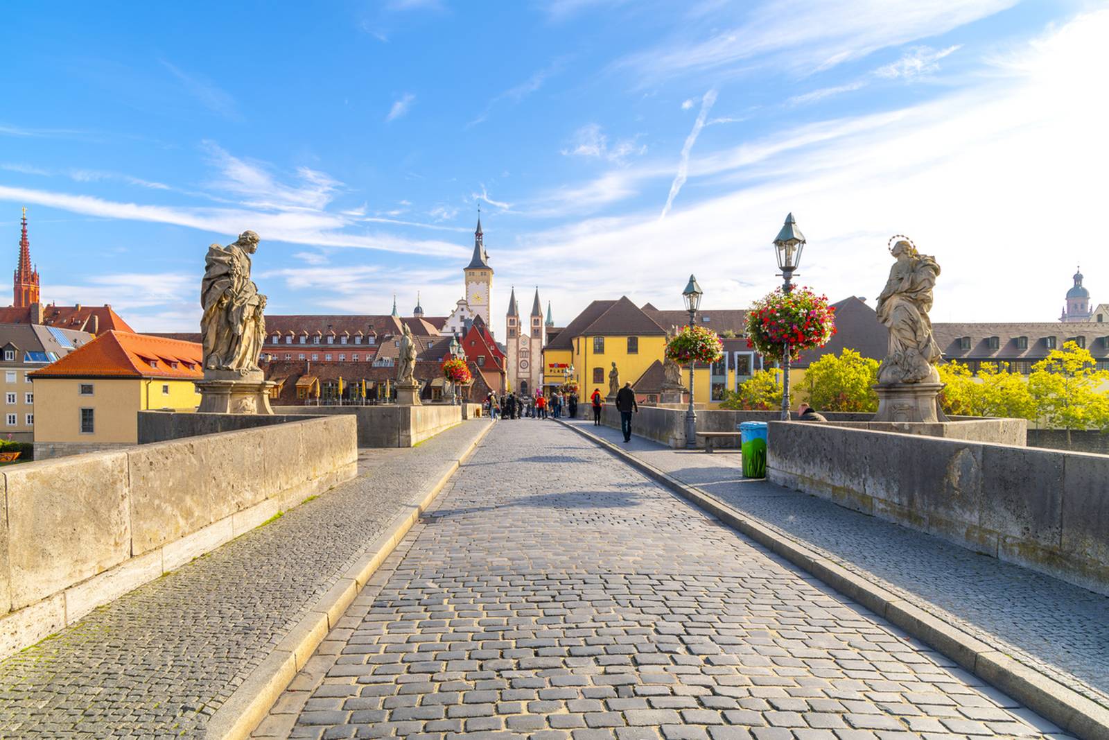 Malerischer Blick auf eine Kopfsteinpflasterbrücke mit Statuen, die zu einer historischen Stadt mit bunten Gebäuden unter blauem Himmel führt