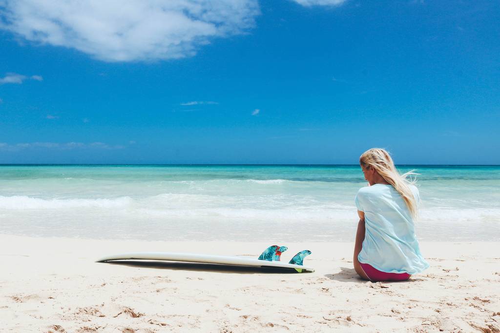 Entspannte Strandstimmung: eine Person genießt die türkisfarbenen Wellen, während das Surfbrett in der Sonne ruht.