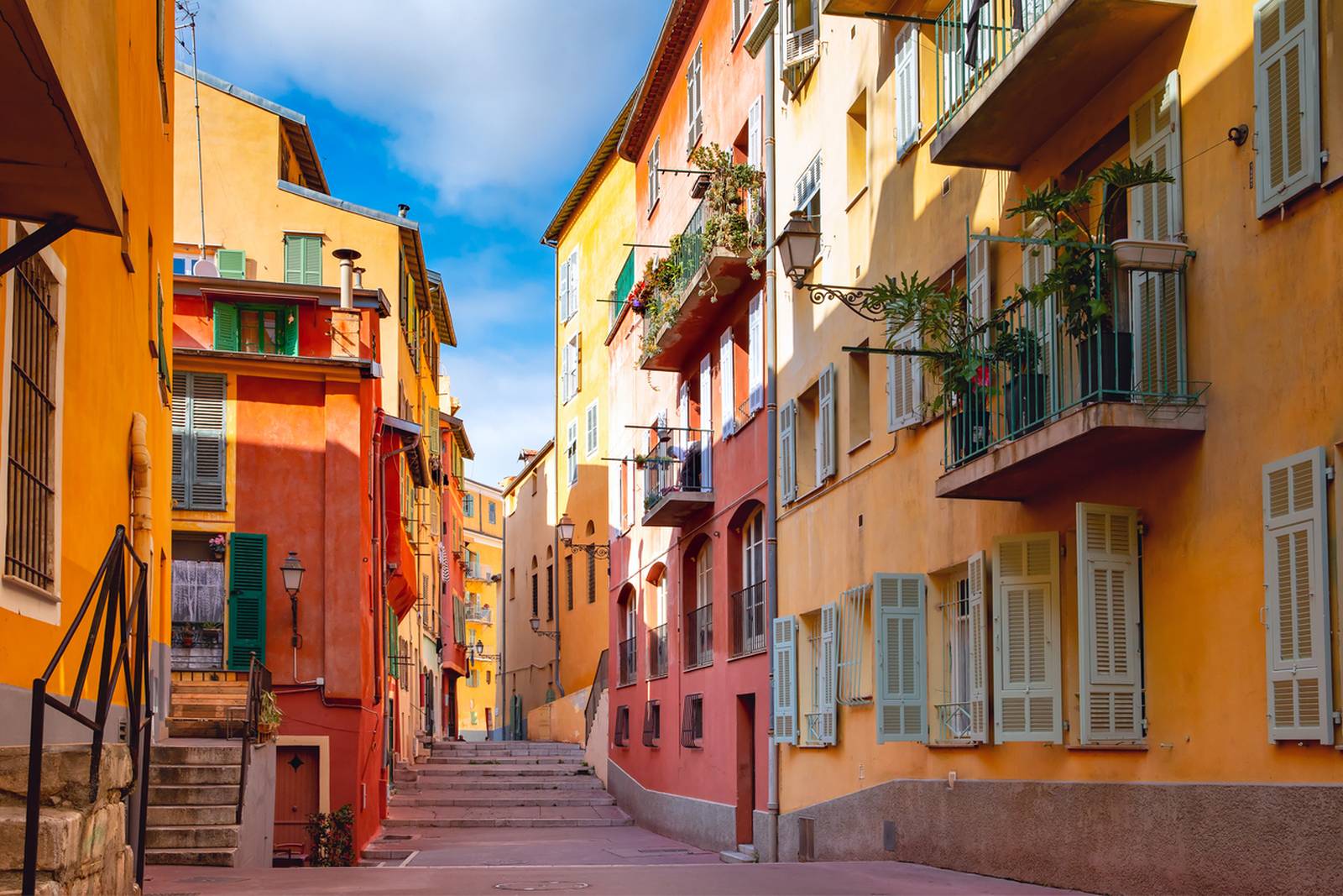 Eine schmale Straße, gesäumt von bunten Häusern mit Balkonen und Fensterläden, unter klarem blauen Himmel