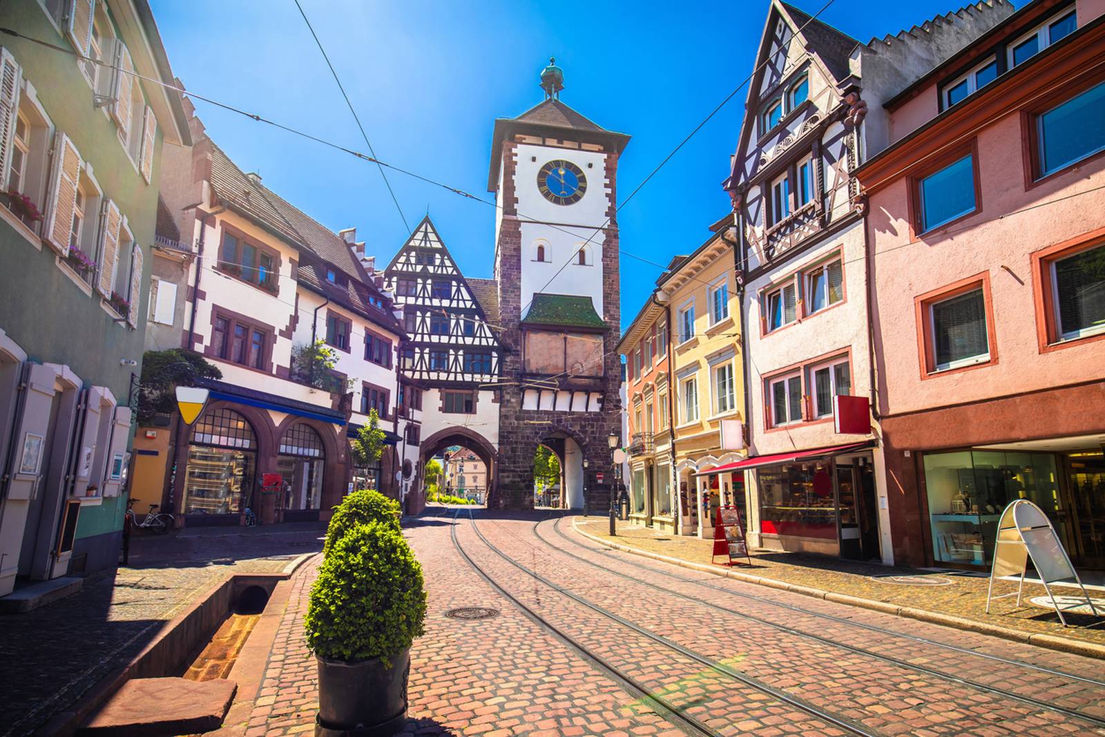 Eine malerische europäische Straße mit bunten Gebäuden, einem Uhrenturm und Straßenbahnschienen unter klarem blauen Himmel