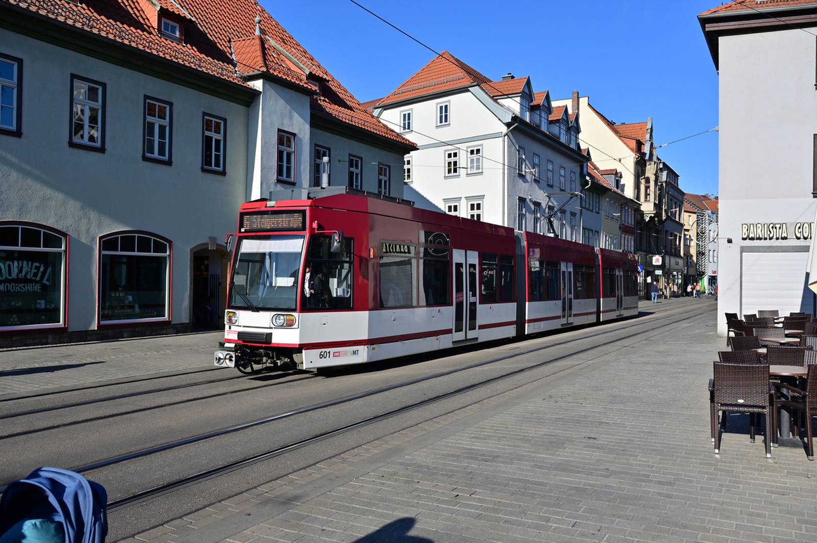 Rot-weiße Straßenbahn fährt auf einer von historischen Gebäuden gesäumten Straße unter klarem blauen Himmel