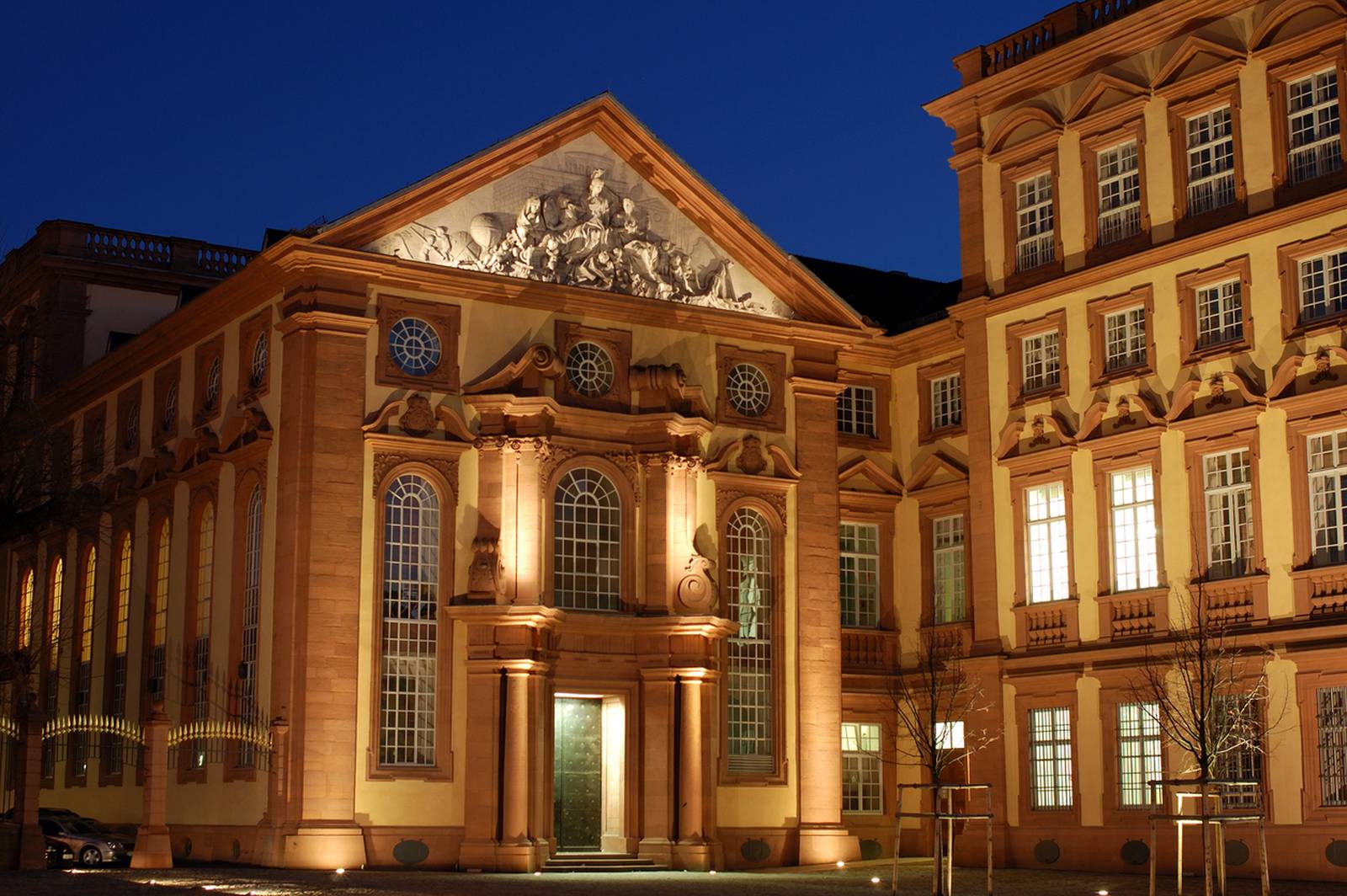 Beleuchtetes Gebäude im Barockstil mit verzierter Fassade und großen Fenstern vor tiefblauem Abendhimmel