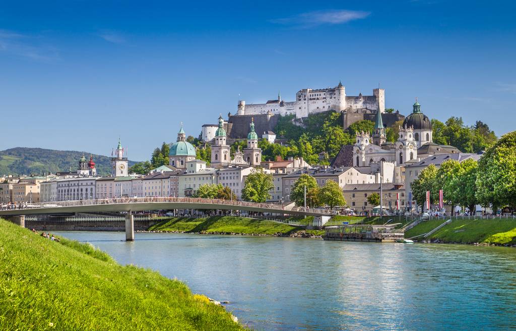 Malerischer Blick auf Salzburg, Österreich, mit der Festung Hohensalzburg auf einem Hügel, historischen Gebäuden, einer Brücke und einem Fluss unter klarem blauem Himmel