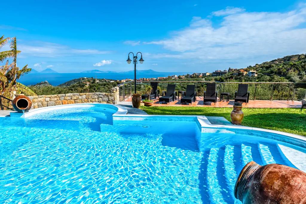 Luxurious pool with steps and a decorative pot, overlooking a scenic landscape with lush greenery and distant mountains under a clear blue sky.