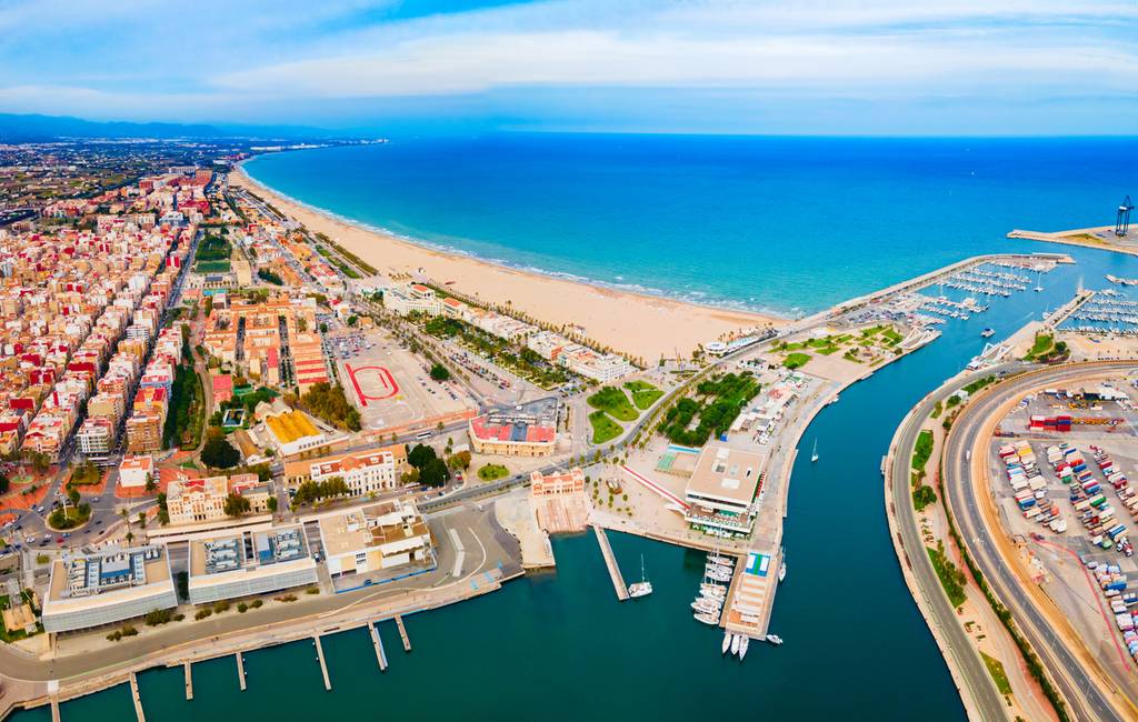 Luftaufnahme einer Küstenstadt mit Sandstrand, Yachthafen und blauem Meer. Städtisches Gebiet auf der linken Seite, Wasser und Boote auf der rechten Seite