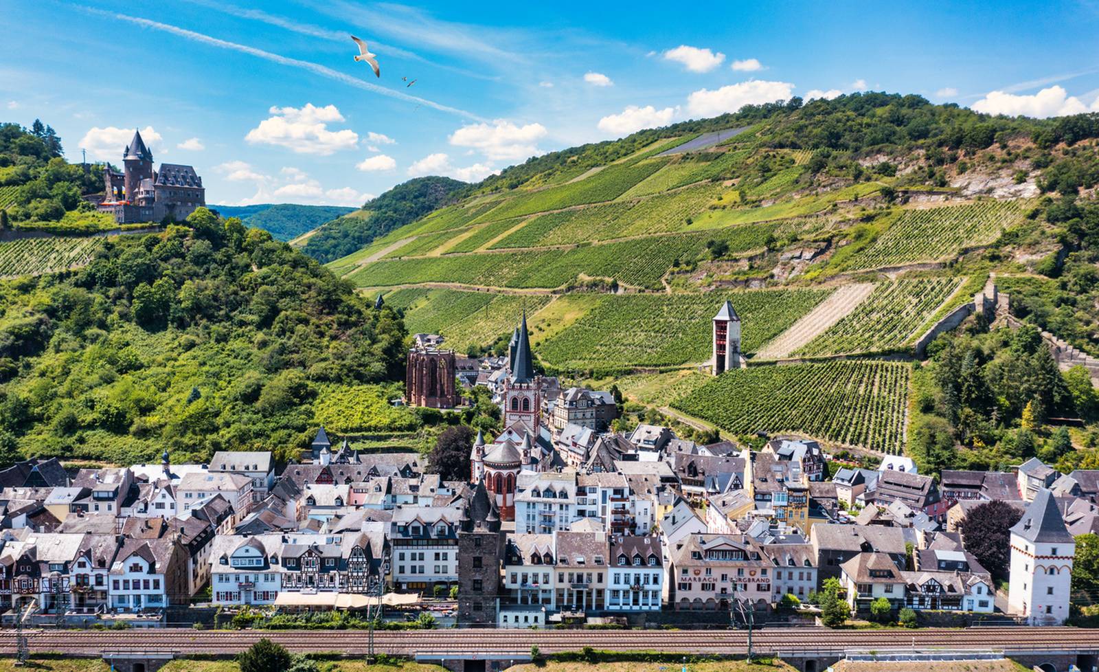 Luftaufnahme eines malerischen Dorfes mit Weinbergen an den Hängen, historischen Gebäuden und einer Kirche unter blauem Himmel mit vereinzelten Wolken