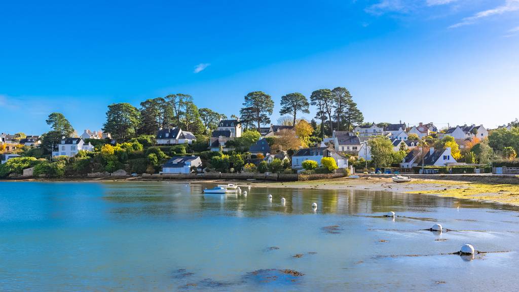 Village côcier aux charmantes maisons, entouré d'arbres, surplombant une baie bleue et paisible parsemée de petits bateaux,