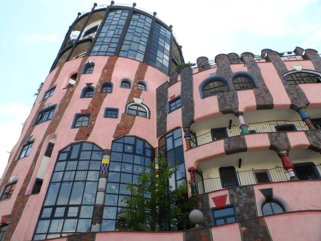 Ein farbenfrohes, verspieltes Gebäude mit pinkfarbenen Wänden, unregelmäßigen Fenstern und einer Mischung aus runden und kantigen Formen, gestaltet in einem fantasievollen Architekturstil
