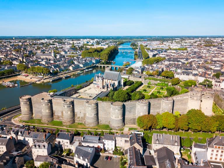 Luftaufnahme einer historischen Burg mit runden Türmen, umgeben von einem Fluss und einer Stadtlandschaft