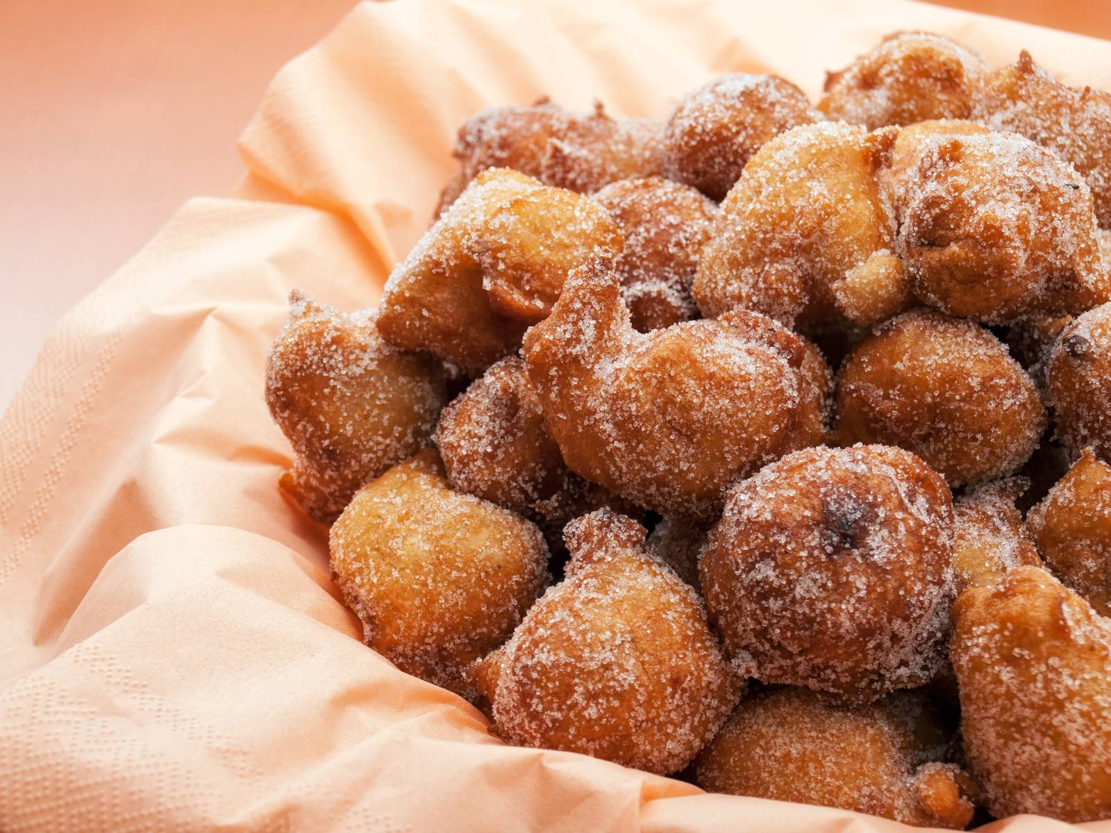 Makroaufnahme von goldbraunen, zuckerbestreuten frittierten Teigstücken, die in einem papierausgelegten Korb gestapelt sind, warm und knusprig, realistisch, detailliert, appetitlich.