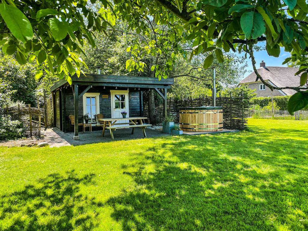 Huisje in een groene tuin met hot tub op het terras