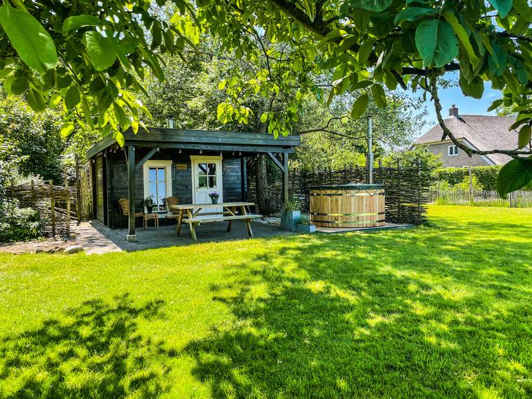 Huisje in een groene tuin met hot tub op het terras