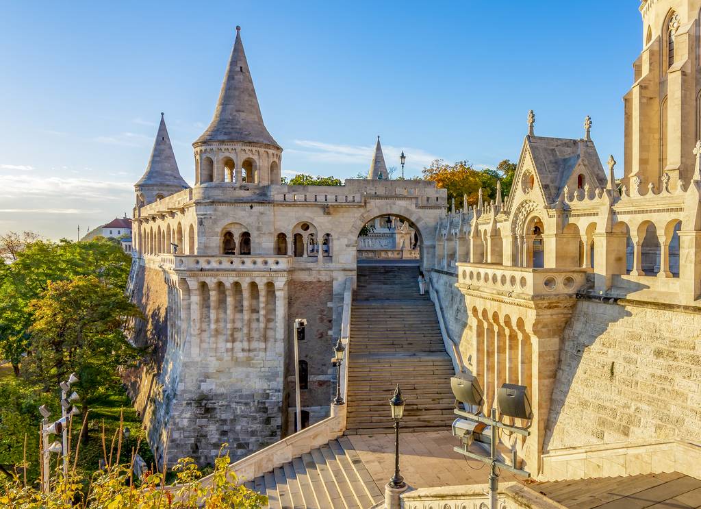 Fisherman's Bastion in Budapest features medieval-style towers and arches, with a staircase leading upward, bathed in warm sunlight.