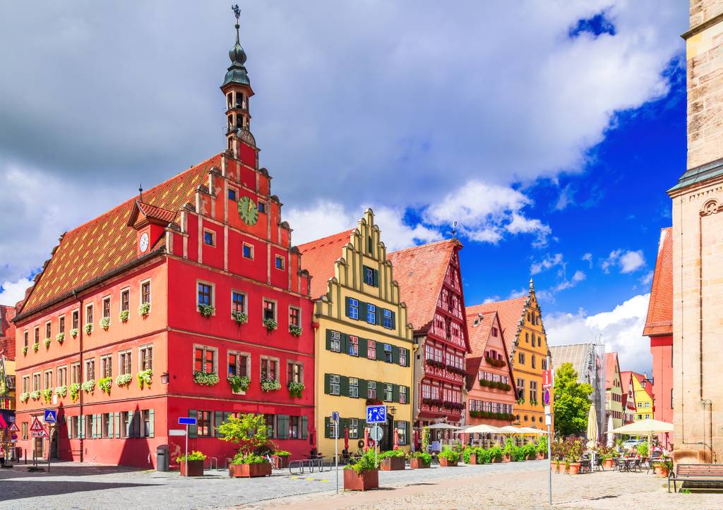 Bunte, historische Gebäude mit verzierten Fassaden säumen eine Kopfsteinpflasterstraße unter einem teilweise bewölkten Himmel in einer malerischen europäischen Stadt.