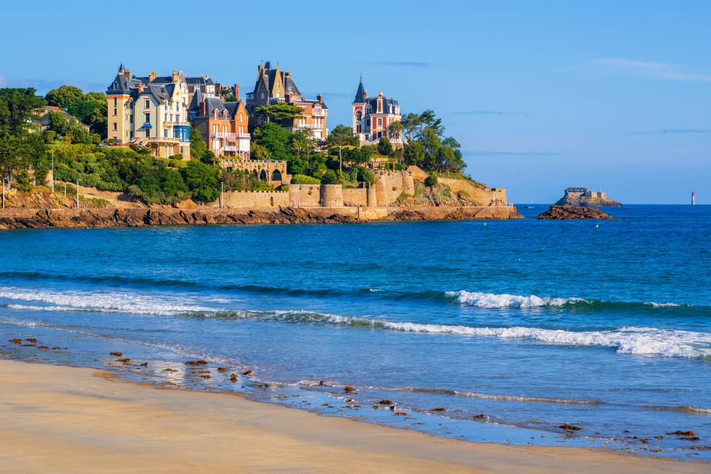 Vue côtière de châteaux élégants et colorés à flanc de falaise, entourés d'une végétation verdoyante, avec une plage de sable, depuis un charmant B&B.