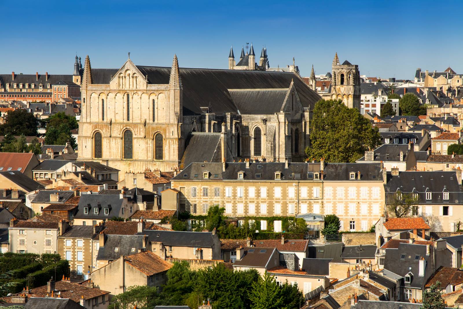 Aerial view of a historic cathedral surrounded by rooftops in a European city, under a clear blue sky.