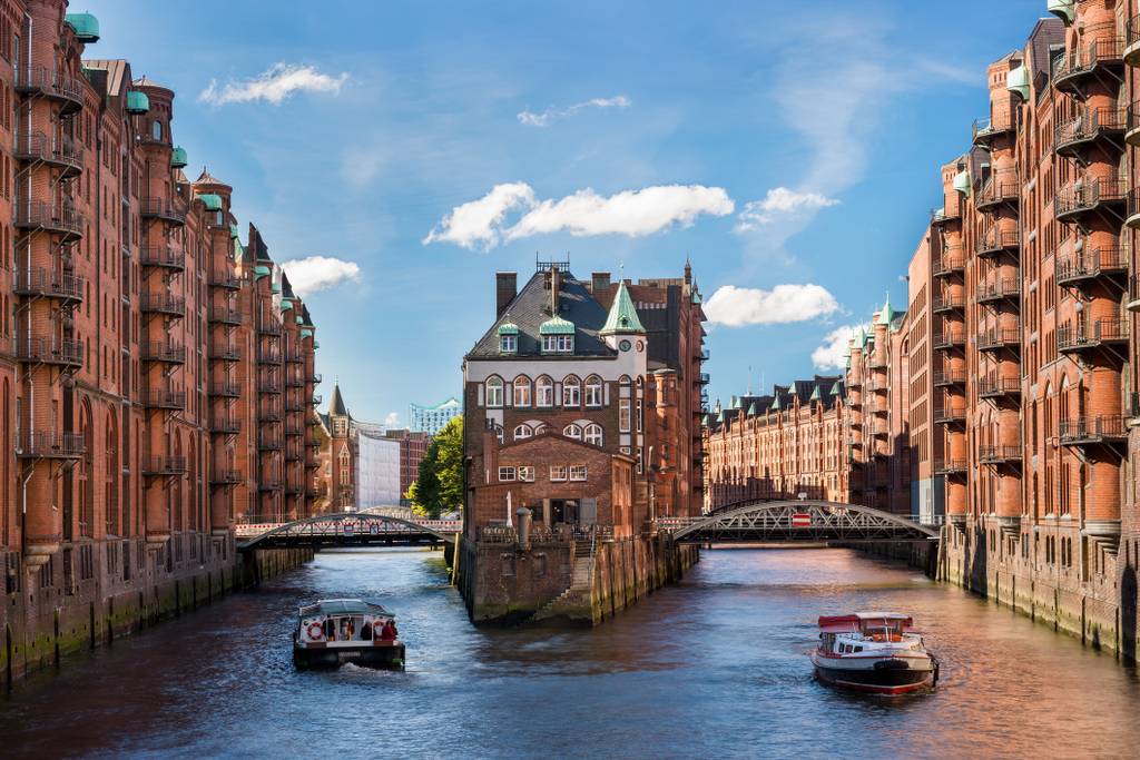 Historic red-brick warehouses lining a canal with a central triangular building and two boats cruising through.
