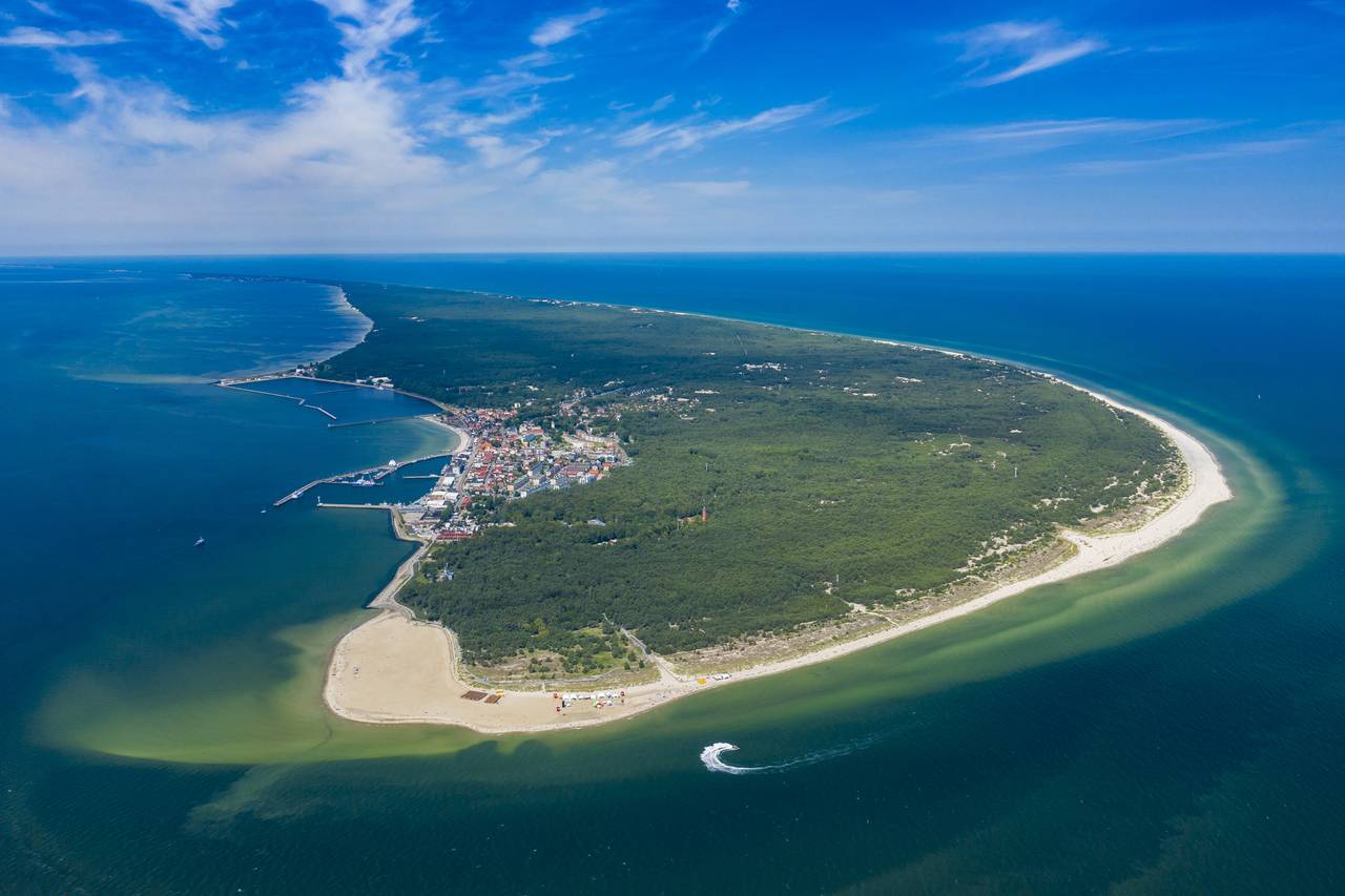 Luftaufnahme einer Halbinsel an der Küste mit üppigem Grün, Sandstränden und einer kleinen Stadt, umgeben von blauem Meer unter klarem Himmel.