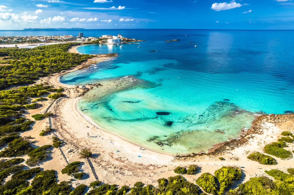 Veduta aerea di Es Trenc , una baia turchese con spiagge di sabbia, vegetazione lussureggiante e l'orizzonte sullo sfondo sotto un cielo azzurro limpido