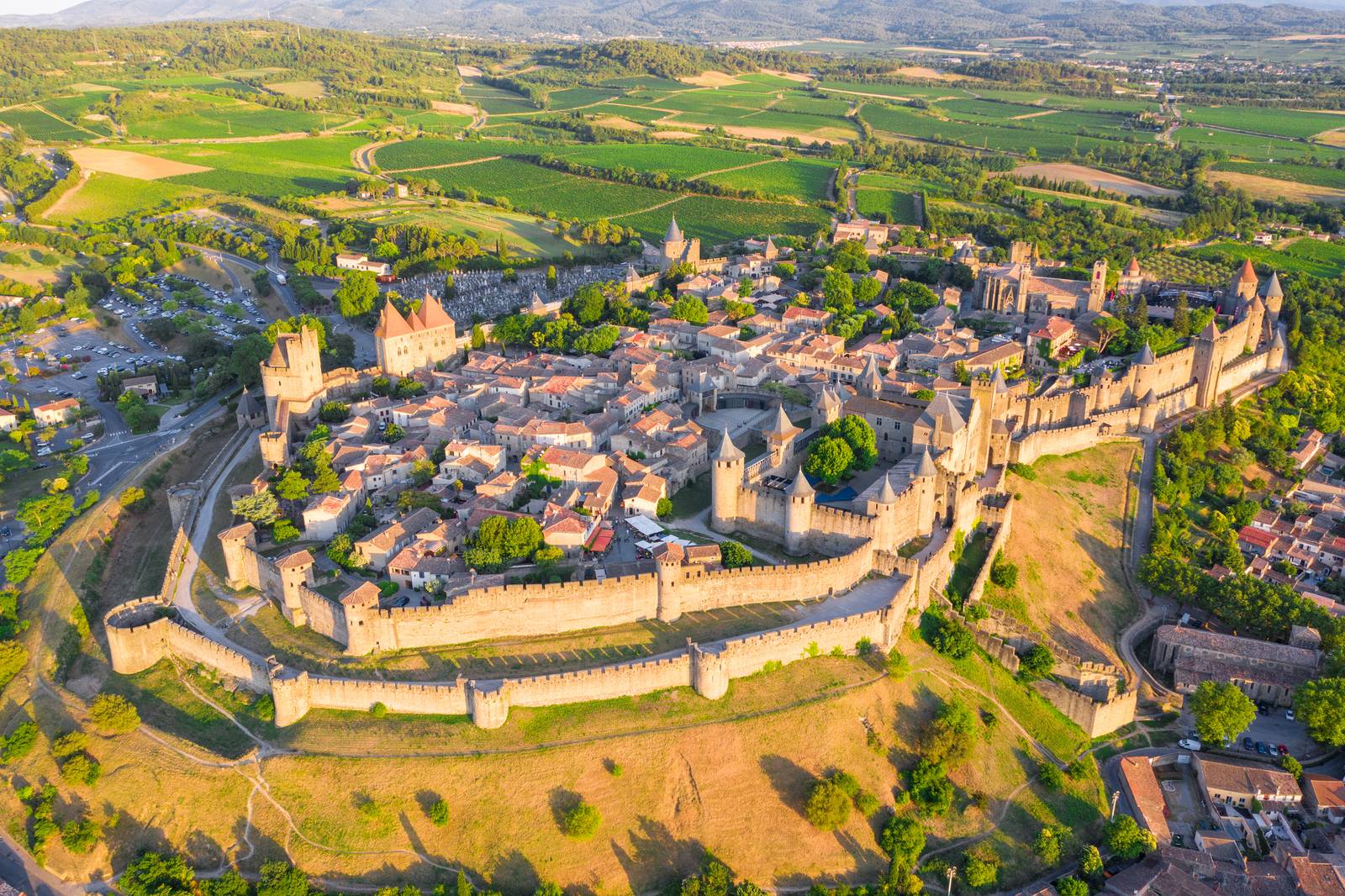 Aerial view of Carcassonne medieval fortress with towers and walls, surrounded by lush green landscape and fields.