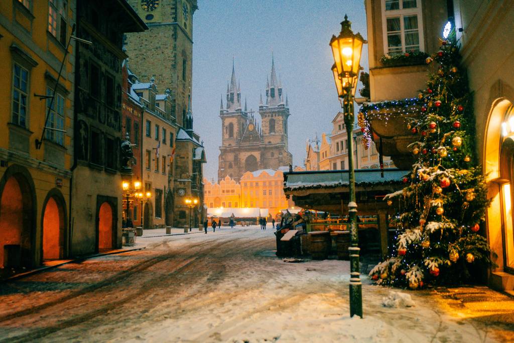 Verschneite Abendstimmung auf einem historischen Marktplatz mit kunstvoll verzierten Straßenlaternen, weihnachtlichen Dekorationen und einer Kirche im Hintergrund.