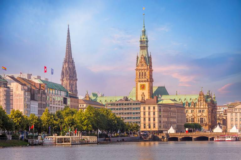 Von der Sonne beschienene Hamburger Hafenpromenade mit dem prächtigen Rathausturm und einem hohen Kirchturm neben den Flussgebäuden.