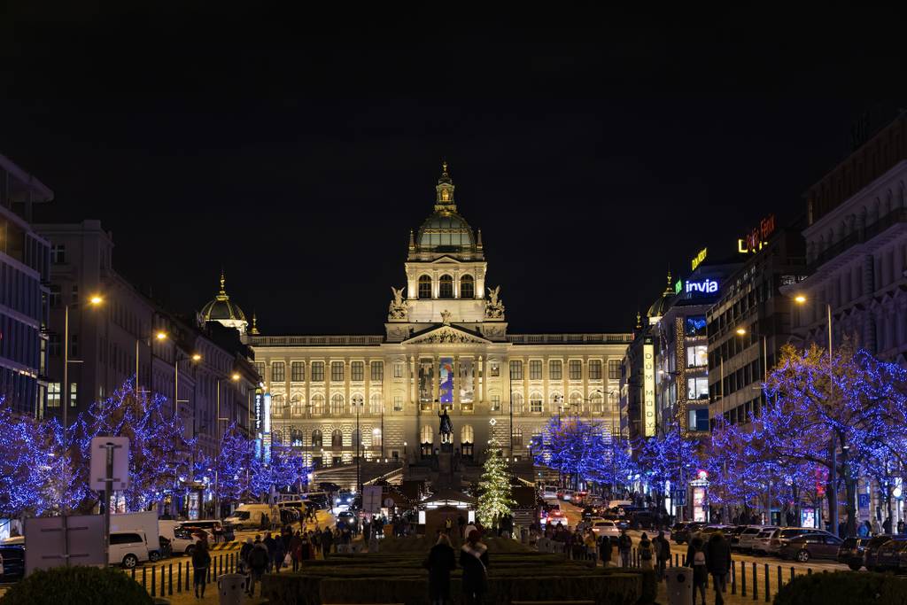 Beleuchtetes Gebäude bei Nacht mit einem erleuchteten Weihnachtsbaum und blau beleuchteten Bäumen entlang einer belebten Straße.