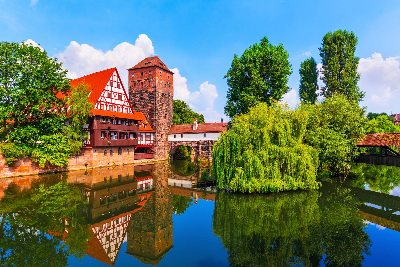Historisches Fachwerkhaus und Steinturm an einem ruhigen Fluss, umgeben von üppigem Grün und klarem, blauem Himmel
