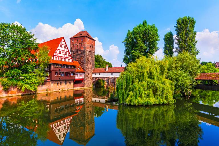 Historisches Fachwerkhaus und Steinturm an einem ruhigen Fluss, umgeben von üppigem Grün und klarem, blauem Himmel